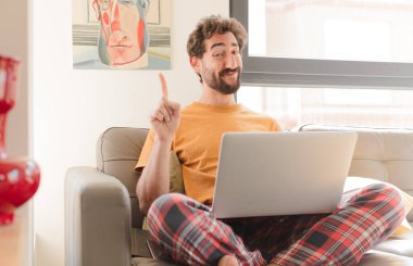 Genç sakallı adam gururla gülümsüyor ve gururla bir numaralı pozu veriyor. Kendini lider gibi hissediyor ve dizüstü bilgisayarla oturuyor.