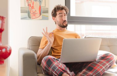 Genç sakallı adam kibirli, başarılı, pozitif ve gururlu görünüyor, kendini gösteriyor ve dizüstü bilgisayarla oturuyor.