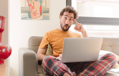 Genç sakallı adam şaşırmış, ağzı açık, şok olmuş, yeni bir düşünce, fikir ya da konsept edinmiş ve dizüstü bilgisayarla oturuyor.