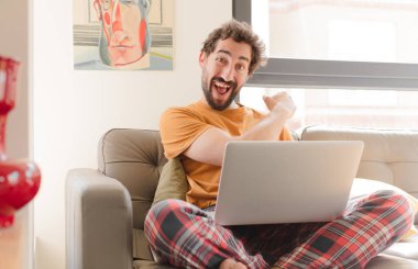 Genç sakallı adam mutlu, pozitif ve başarılı hissediyor, bir meydan okumayla karşılaştığında ya da iyi sonuçları kutlarken ve dizüstü bilgisayarla otururken motive oluyor.