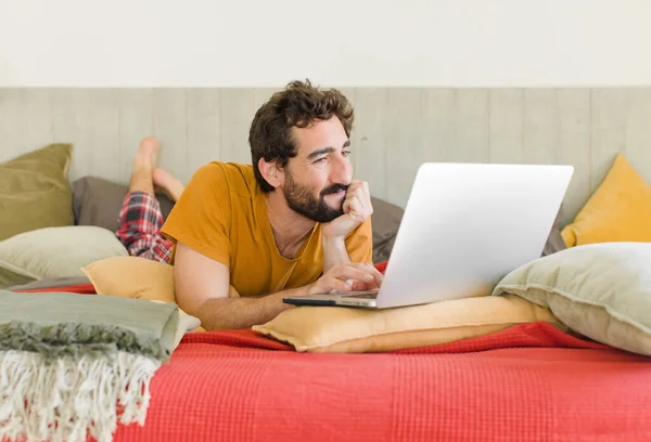 young bearded man on a bed with a laptop