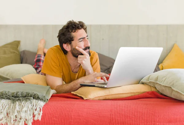 young bearded man on a bed with a laptop