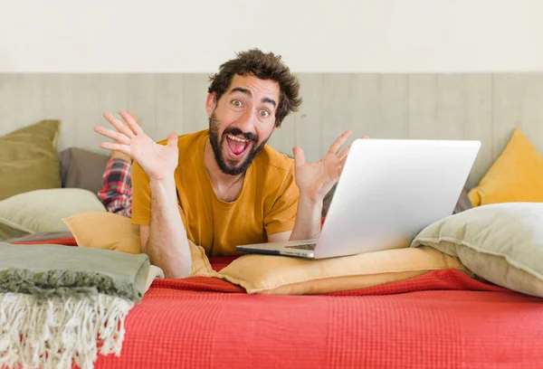 young bearded man on a bed with a laptop