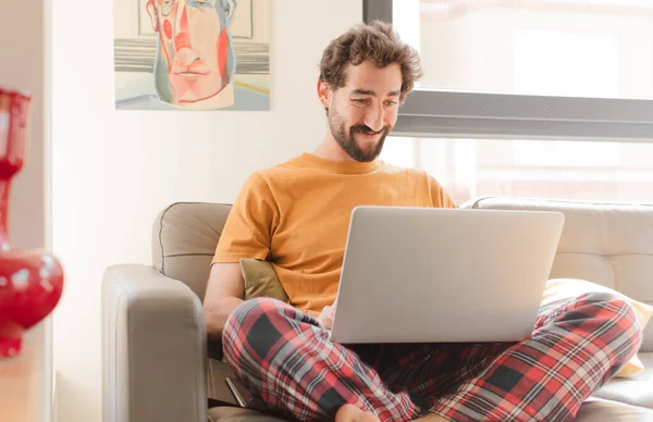 young bearded man on a couch with a laptop