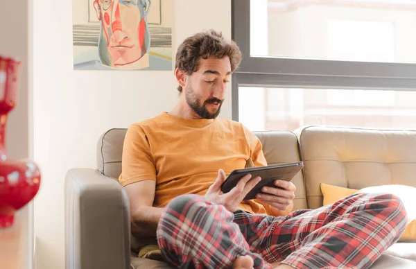 Kanepedeki sakallı genç adam Dokunmatik ekranlı tabletle