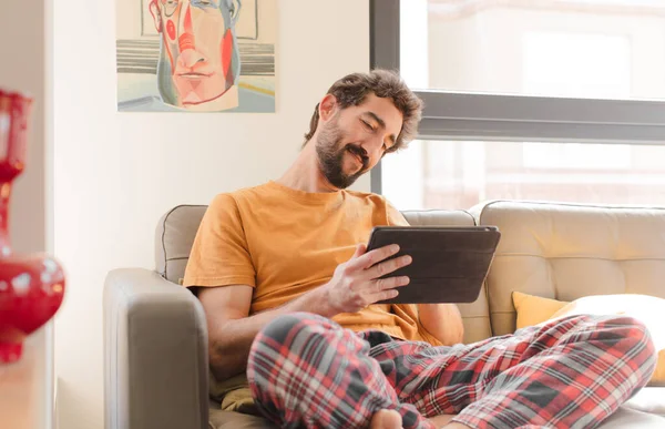 Kanepedeki sakallı genç adam Dokunmatik ekranlı tabletle