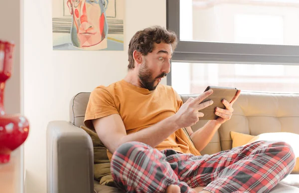 Kanepedeki sakallı genç adam Dokunmatik ekranlı tabletle