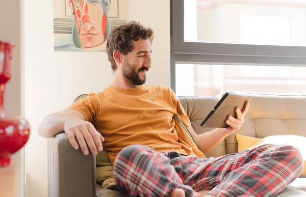 Kanepedeki sakallı genç adam Dokunmatik ekranlı tabletle