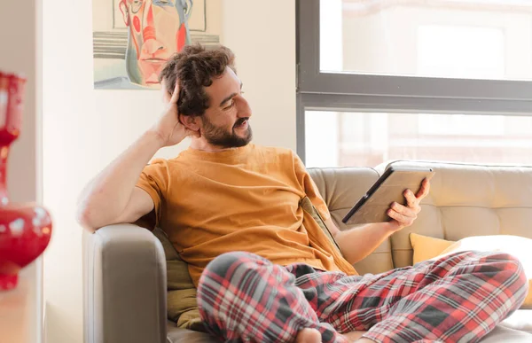 Kanepedeki sakallı genç adam Dokunmatik ekranlı tabletle