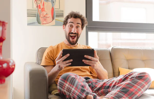 Kanepedeki sakallı genç adam Dokunmatik ekranlı tabletle