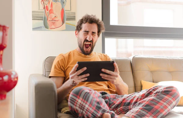 Kanepedeki sakallı genç adam Dokunmatik ekranlı tabletle