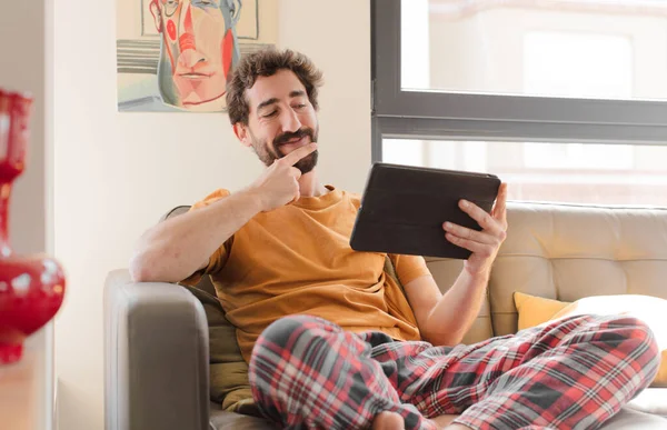 Kanepedeki sakallı genç adam Dokunmatik ekranlı tabletle