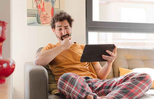 Kanepedeki sakallı genç adam Dokunmatik ekranlı tabletle