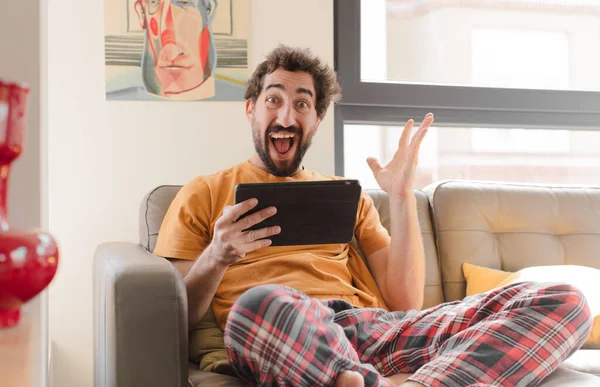 Kanepedeki sakallı genç adam Dokunmatik ekranlı tabletle