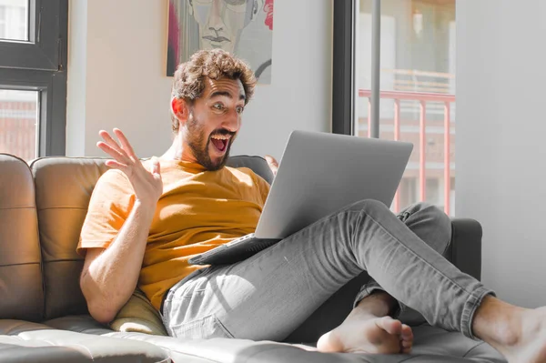 Genç sakallı adam mutlu, heyecanlı, şaşırmış ya da şok olmuş hissediyor. Kanepe dizüstü bilgisayarında inanılmaz bir şeye gülümsüyor ve hayrete düşüyor.