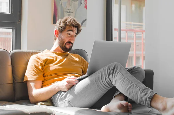 Genç sakallı bir adam üzgün ve mızmız görünüyor. Ağlıyor. Kanepe dizüstü bilgisayarında dizüstü bilgisayarla olumsuz ve hayal kırıklığına uğramış bir tavırla.