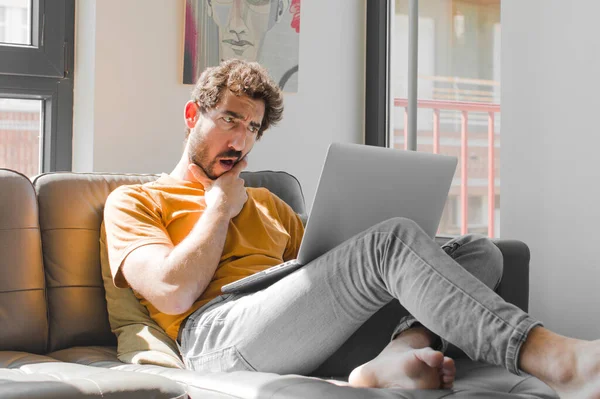 Ağzı ve gözleri açık genç sakallı bir adam, elleri çenesinde, kötü bir şok geçiriyor, dizüstü bilgisayar konseptinde dizüstü bilgisayarla ne söylüyor ya da vay be diyor.