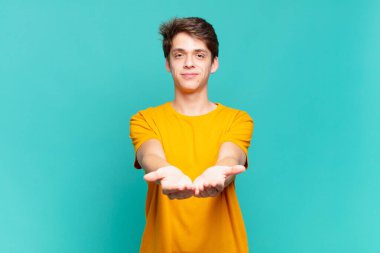 Genç çocuk mutlu bir şekilde gülümsüyor arkadaş canlısı, kendinden emin, pozitif bakışlı, bir nesne ya da konsept sunuyor ve gösteriyor