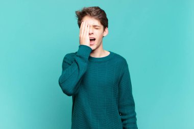 Genç çocuk uykulu, sıkılmış ve esniyor, baş ağrısı ve yüzünün yarısını kaplayan bir elle.