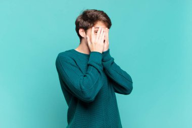 Genç bir çocuk korkmuş ya da utanmış hissediyor. Gözleri yarı kapalı ya da ellerle dikizliyor ya da dikizliyor.