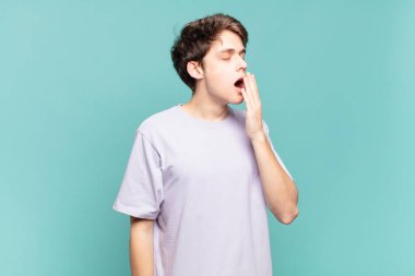 Genç bir çocuk sabahın erken saatlerinde uykulu, yorgun ve sıkkın bir şekilde esniyor.