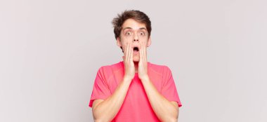 Delikanlı şokta ve korkmuş görünüyor, ağzı açık ve elleri yanaklarında.