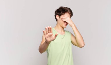 Genç çocuk yüzünü eliyle kapatıyor ve kamerayı durdurmak için diğer elini öne koyuyor, fotoğraf ya da resimleri reddediyor.