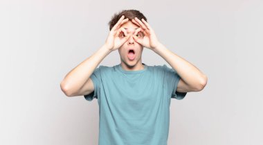 Şok olmuş, şaşırmış ve şaşırmış hisseden genç bir çocuk, elinde şaşkın, inançsız bir bakışla gözlük tutuyor.