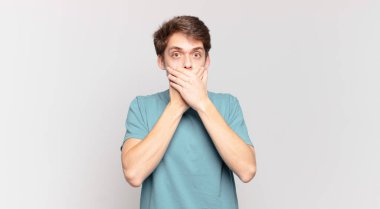 Şok olmuş, şaşırmış bir ifadeyle ağzı kapatan genç bir çocuk sır saklıyor ya da 