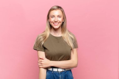 Genç sarışın güzel kadın utangaç ve neşeli bir şekilde gülüyor, arkadaş canlısı ve olumlu ama güvensiz bir tavırla.