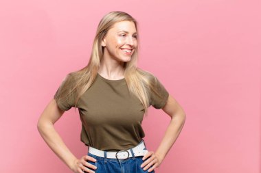 Genç sarışın güzel kadın mutlu, neşeli ve kendinden emin görünüyor gururla gülümsüyor ve iki elini de kalçasında istiyor.