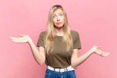 Genç sarışın güzel kadın şaşkın, kafası karışmış ve stresli görünüyor, farklı seçenekler arasında merak ediyor, kararsız hissediyor.