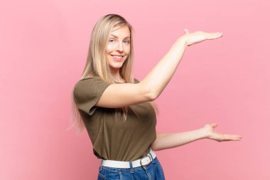 Genç sarışın güzel kadın gülümsüyor, mutlu, pozitif ve tatmin olmuş hissediyor, fotokopi alanında nesne ya da konsept tutuyor ya da gösteriyor