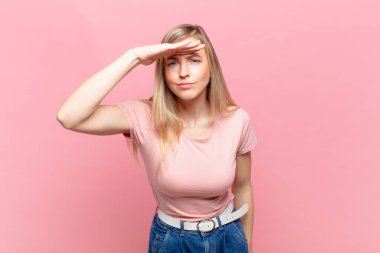 Genç sarışın güzel kadın şaşkınlık ve şaşkınlık içinde bakıyor, el üstünde uzak bakıyor, izliyor ya da arıyor