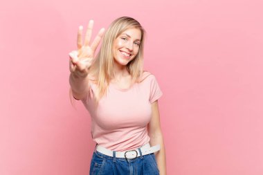 Genç sarışın güzel kadın gülümsüyor ve arkadaş canlısı görünüyor. Üç ya da üç numarayı gösteriyor. Elleri önde, geriye doğru sayıyor.