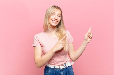 Genç sarışın güzel kadın mutlu bir şekilde gülümsüyor ve her iki elinde fotokopi uzayında nesne gösteriyor.