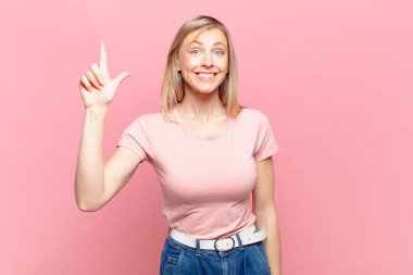 Genç, sarışın, güzel bir kadın. Neşeli ve mutlu bir şekilde gülümsüyor. Bir eliyle uzayı işaret ediyor.