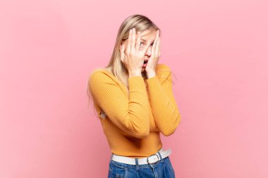 Genç, sarışın, güzel bir kadın korkmuş ya da utanmış hissediyor. Gözleri yarı kapalı ya da ellerle dikizliyor ya da dikizliyor.