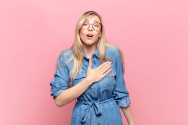 Genç sarışın, güzel bir kadın şok olmuş ve şaşırmış hissediyor, gülümsüyor, el ele tutuşuyor, mutlu ya da şükran duyuyor.