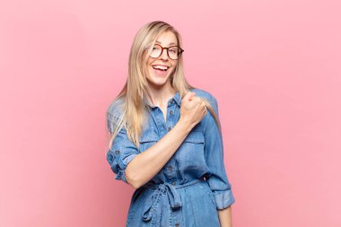 Genç sarışın güzel kadın mutlu, pozitif ve başarılı hissediyor, meydan okumayla karşılaştığında motive oluyor ya da iyi sonuçları kutluyor.