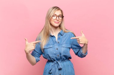 Genç sarışın güzel kadın gururlu, pozitif ve rahat görünüyor. İki eliyle göğsünü gösteriyor.