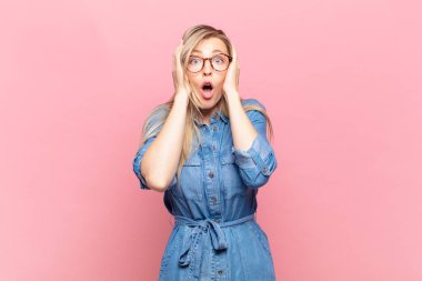 Genç sarışın güzel kadın hoş olmayan bir şekilde şoka uğramış, korkmuş ya da endişeli görünüyor ağzı sonuna kadar açık ve iki kulağını da elleriyle kapatıyor.