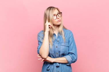 Genç sarışın, güzel bir kadın. Yoğunlaşmış bakışları var. Şüpheli bir ifadeyle yukarı ve yana bakıyor.