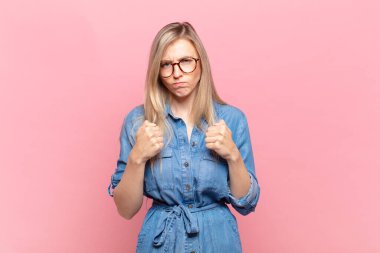 Genç sarışın güzel bir kadın kendinden emin, sinirli, güçlü ve agresif görünüyor. Yumrukları boks pozisyonunda dövüşmeye hazır.