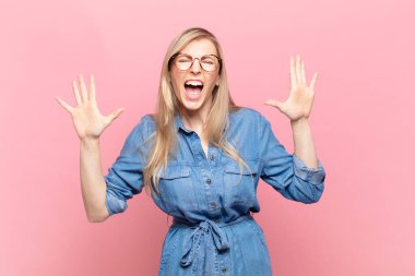 Genç sarışın güzel bir kadın panik ya da öfke içinde bağırıyor, şok olmuş, korkmuş ya da öfkeli, elleri başının yanında.