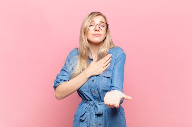 Genç sarışın güzel bir kadın mutlu ve aşık, bir eli kalbinin yanında, diğer eli önde uzanmış, gülümsüyor.