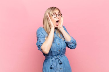 Genç sarışın güzel bir kadın mutlu, heyecanlı ve şaşırmış hissediyor. İki eli de havada bir tarafa bakıyor.