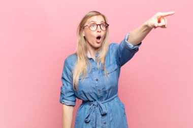 Genç sarışın, güzel bir kadın şok olmuş ve şaşırmış hissediyor. Şaşkın ve açık ağızlı bir bakışla yukarılara bakıyor ve işaret ediyor.