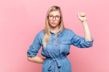 Genç sarışın güzel kadın ciddi, güçlü ve asi hissediyor, yumruğunu kaldırıyor, protesto ediyor ya da devrim için savaşıyor.