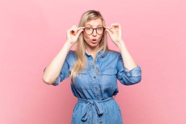 Genç sarışın güzel kadın şok olmuş, şaşırmış ve şaşırmış hissediyor, elinde şaşkın, inançsız bir bakışla gözlük tutuyor.